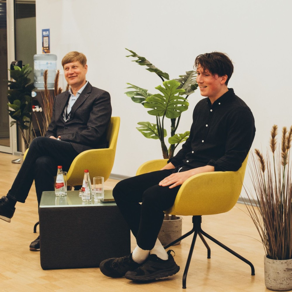 1728549515815 divi vīrieši sēž zāles priekšā